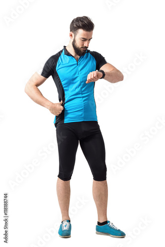 Sport cycling athlete in blue jersey shirt checking time on wristwatch. Full body length portrait isolated over white studio background.