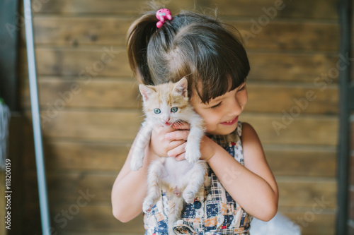 cheerful little girl holding a frightened cat in hands