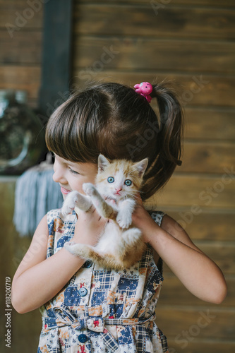 cheerful little girl holding a frightened cat in hands