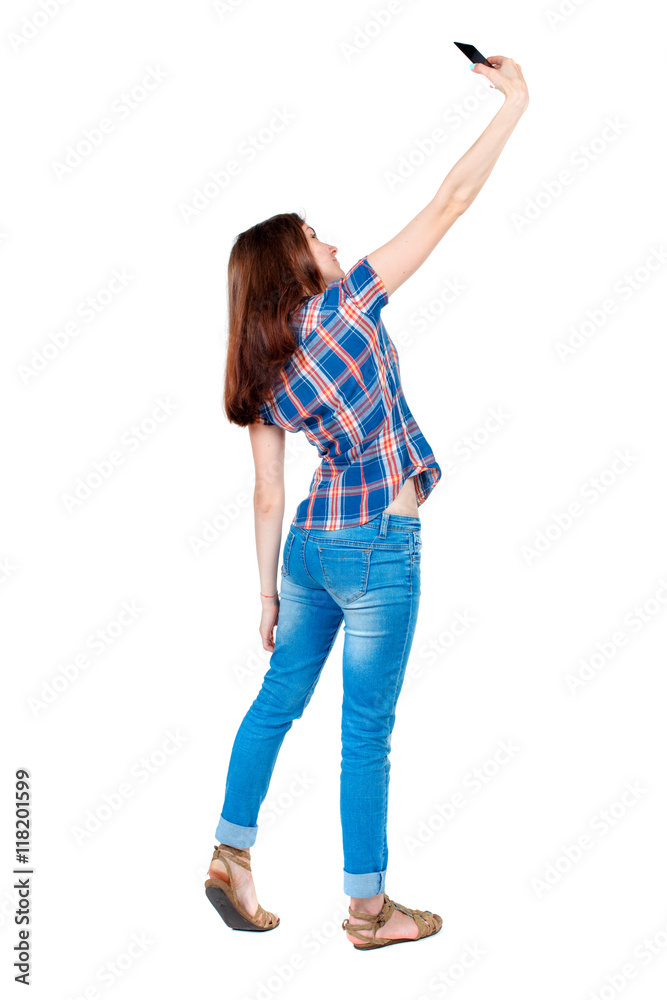 back view of standing young beautiful woman using a mobile phone. girl watching. Rear view people collection. backside view of person. Isolated over white background. Girl in a plaid shirt is back view of standing young beautiful woman using a mobile phone. girl watching. Rear view people collection. backside view of person. Isolated over white background. Girl in a plaid shirt is