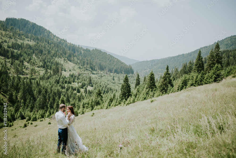 Vintage wedding photography of a young hipster couple curly bride posing at sunset in the forest and mountains dressed in a suite and white dress