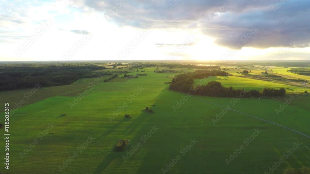 Stunning aerial shot over lush green fields and meadows in the Estonian countryside. It is a clear, bright summer day and the sun is shining. Sunset. Stunning aerial shot over lush green fields and meadows in the Estonian countryside. It is a clear, bright summer day and the sun is shining. Sunset.