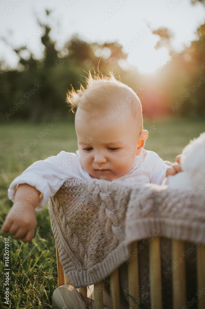 Cute baby boy and his toy playing in a wooden box making funny and happy faces warm summer sunset in the park