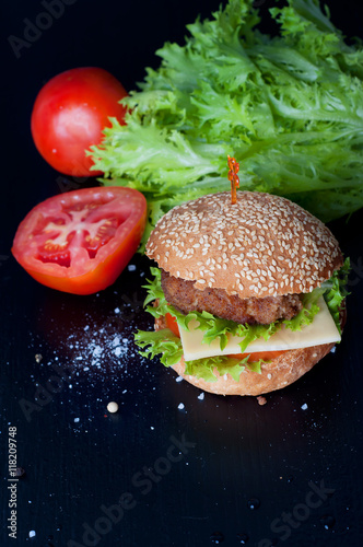 Hamburger with salad, tomato, meat on black  backdrop