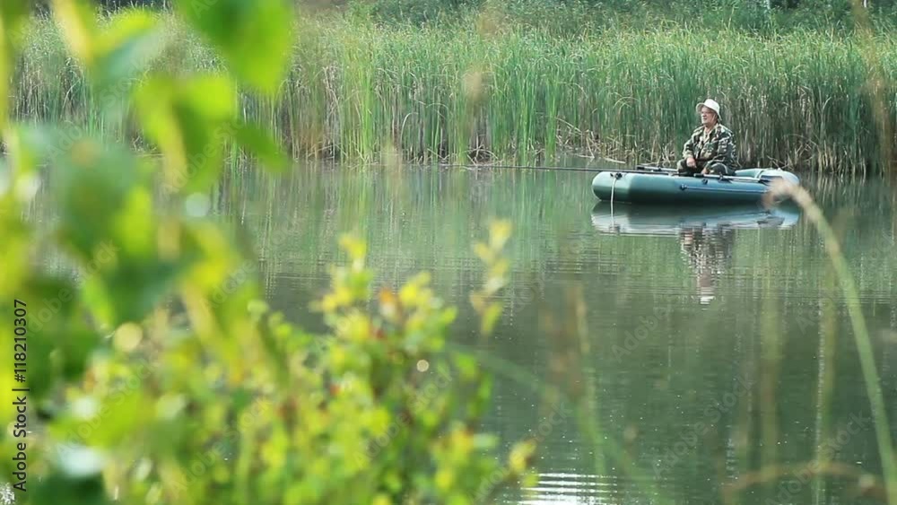The fisherman floats on a lake on an inflatable boat with a fishing rod. Early morning with fog on the water. vacation in the wild The fisherman floats on a lake on an inflatable boat with a fishing rod. Early morning with fog on the water. vacation in the wild