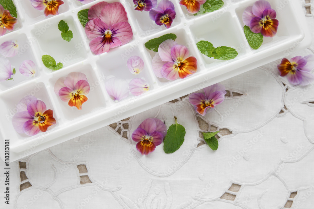 Edible flowers and mint in ice cubes tray on white vintage linen Edible flowers and mint in ice cubes tray on white vintage linen