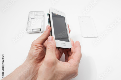 Smartphone dismantling on white background. Repairman hands holding telephone in hands. Disassembled phone in repair service, white background, electronics recovery concept
