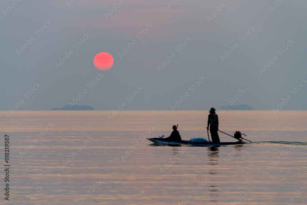Naklejka premium Fishermen in a boat looking at the setting sun 