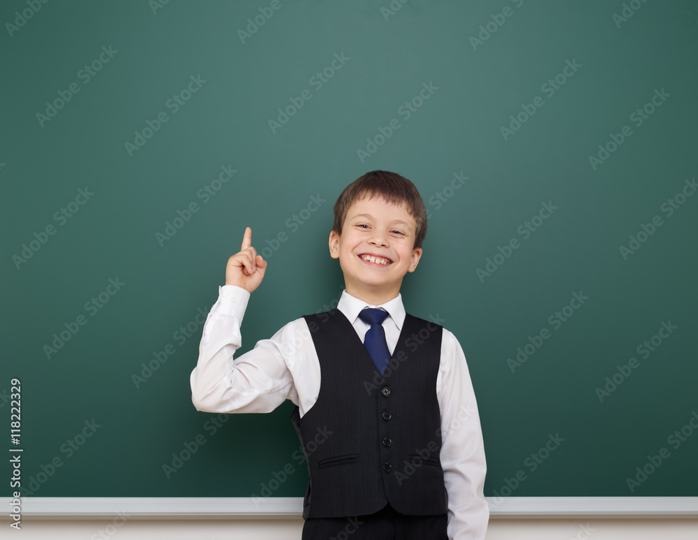 school student boy posing at the clean blackboard, show finger up and point, grimacing and emotions, dressed in a black suit, education concept, studio photo