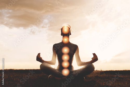 Woman practicing meditation in sunset, with chakras marked © Tijana