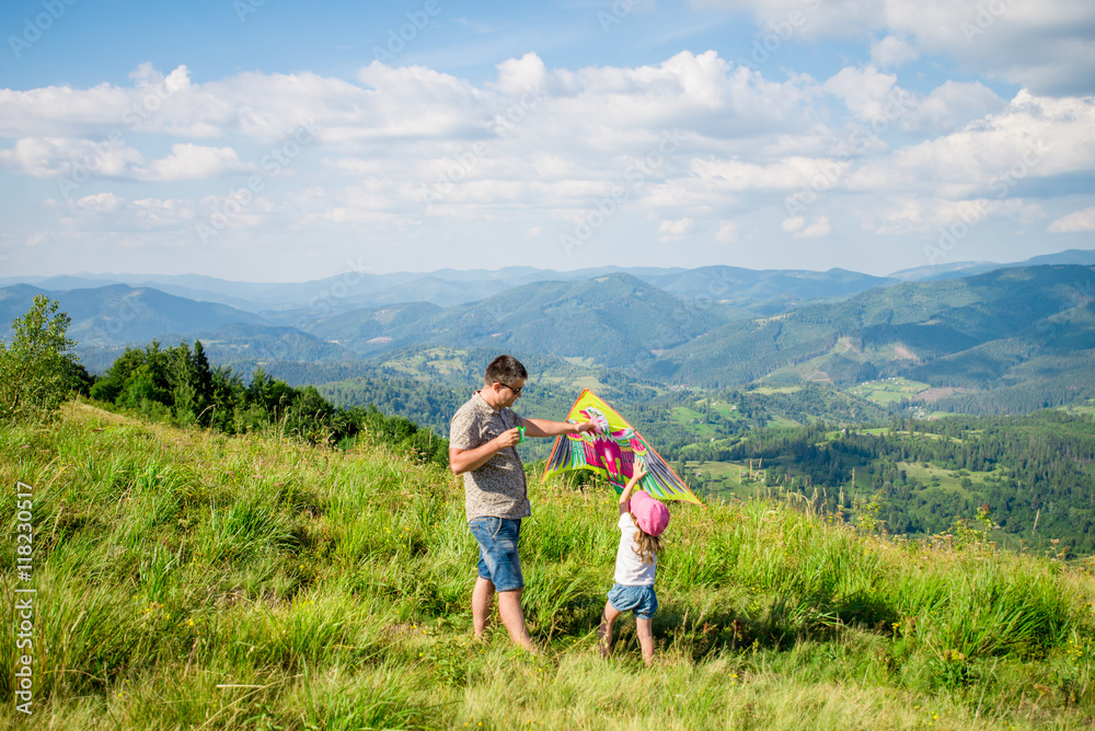 Dad and daughter launch a kite against the backdrop of beautiful views of mountains and sky. Horizontal