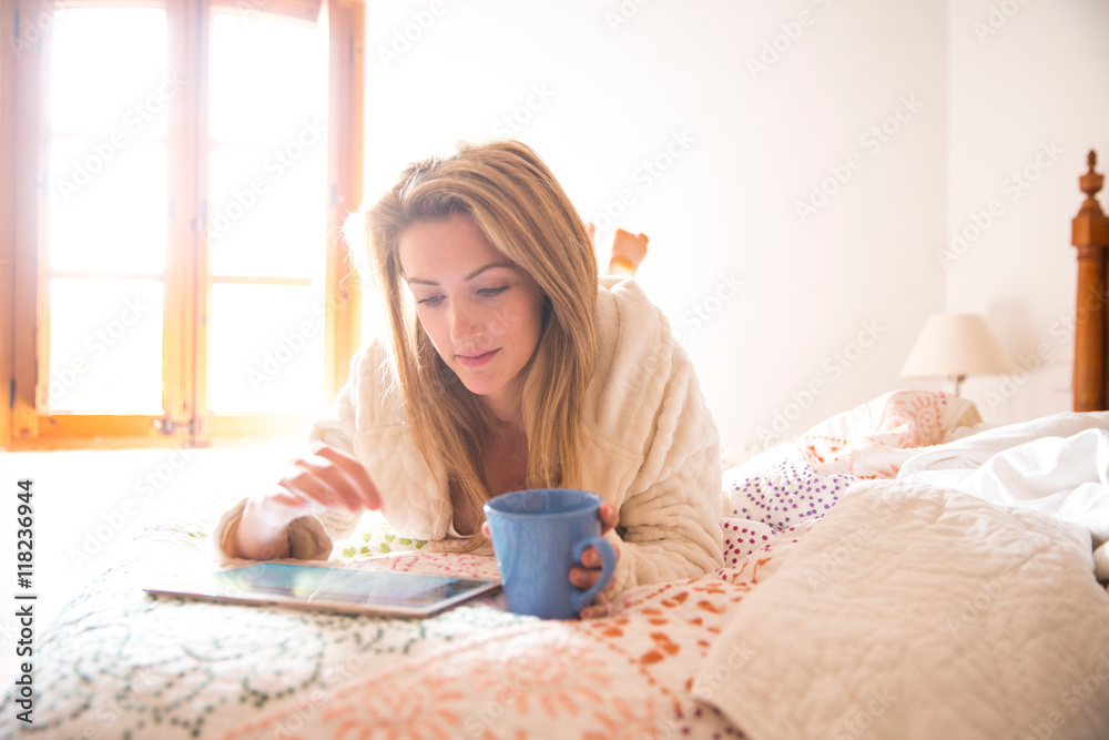 Young woman lying on bed browsing digital tablet in morning Young woman lying on bed browsing digital tablet in morning