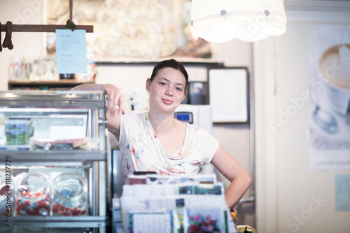 Portrait of young female shop assistant leaning on corner shop counter