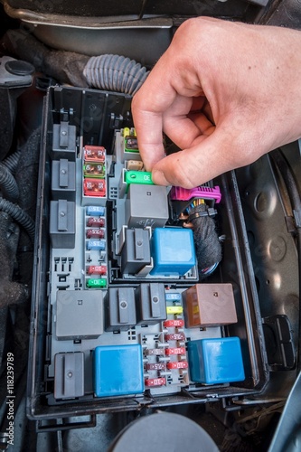 Hand checking a fuse in the fuse box of a modern car engine