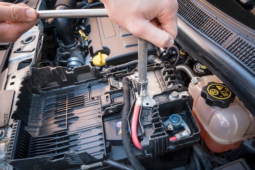 Hands checking the bolt of the battery with a wrench in a modern car engine