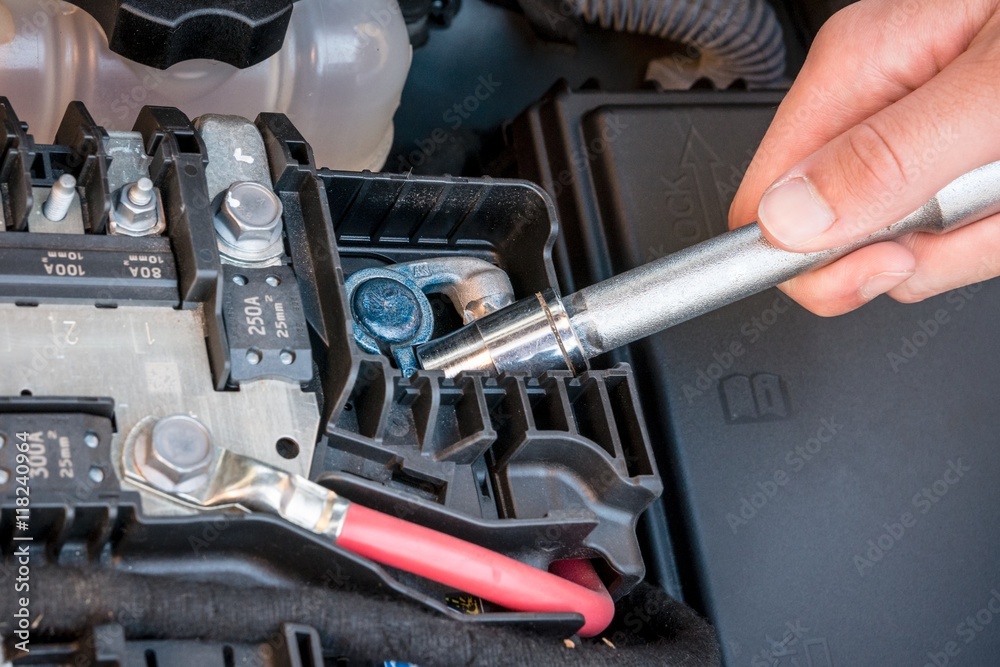 Hand checking the bolt of the battery with a wrench in a modern car engine Hand checking the bolt of the battery with a wrench in a modern car engine