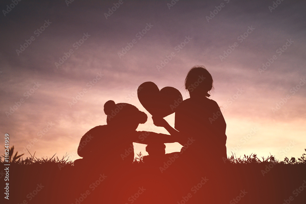 Silhouette girl with teddy bear at sunset.