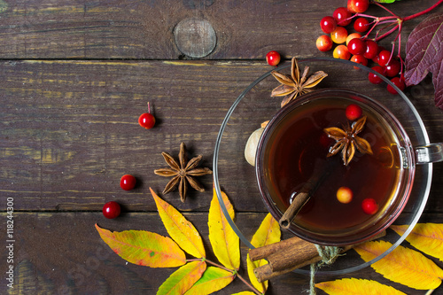 Fototapeta Naklejka Na Ścianę i Meble -  Autumn hot tea with spices and berries in glass cup and falling leaves