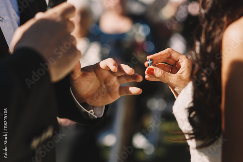Bride holds a silver wedding ring before groom's face