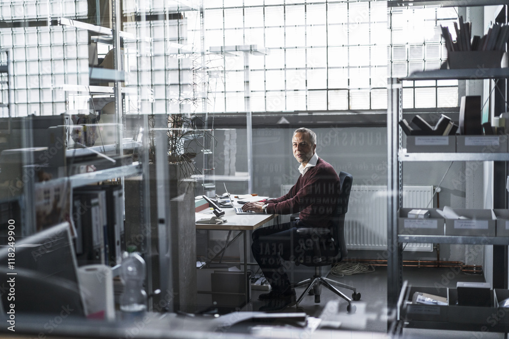 Mature man using laptop at desk in a factory Mature man using laptop at desk in a factory