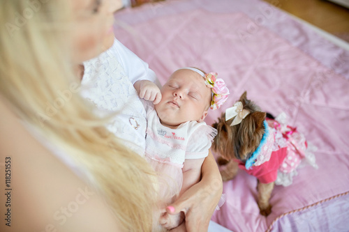 Blonde mom holds her sleepy daughter while little dog plays on t