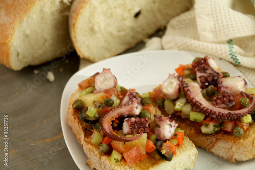 Octopus salad on bruschetta bread. Background: bread, napkin on wooden table.