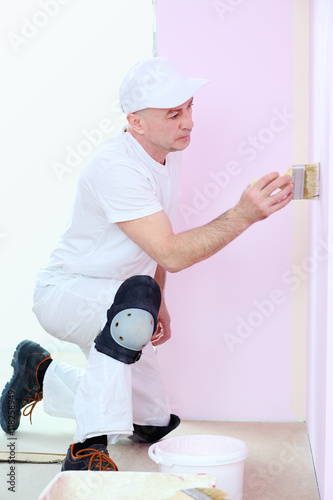 Finisher in white clothes with a brush in hand painted walls in pink room photo