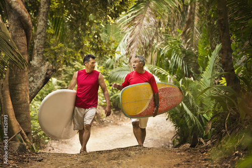 Hispanic men carrying surfboards on jungle trail