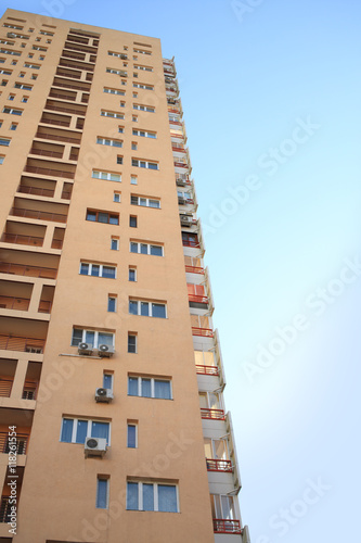 multi-storey building with windows, balconies and air conditioning on background of blue sky
