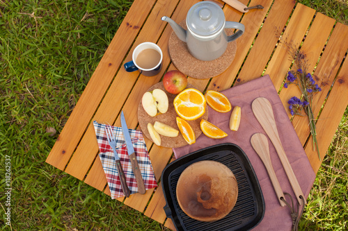 picnic, view of picnic table with various fruits, juice, pancake, coffee and vegetable at the camping area.