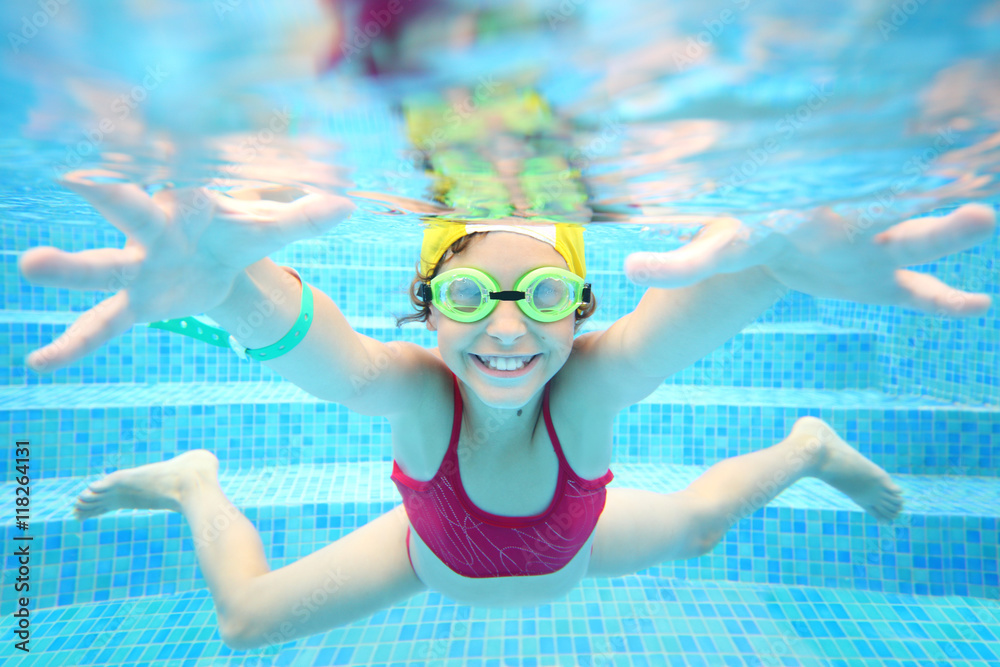 Happy girl in swimming glasses under water in the pool