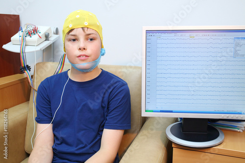 Boy in a special cap during electroencephalography next to the monitor with readings photo