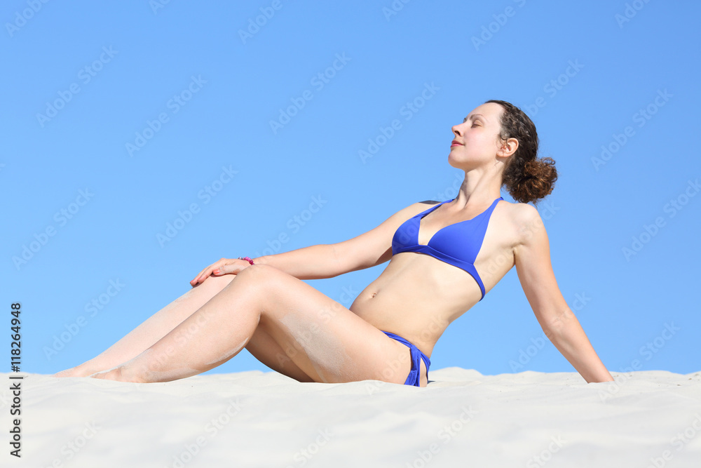 Pretty attractive woman in blue bikini sitting on a sandy beach