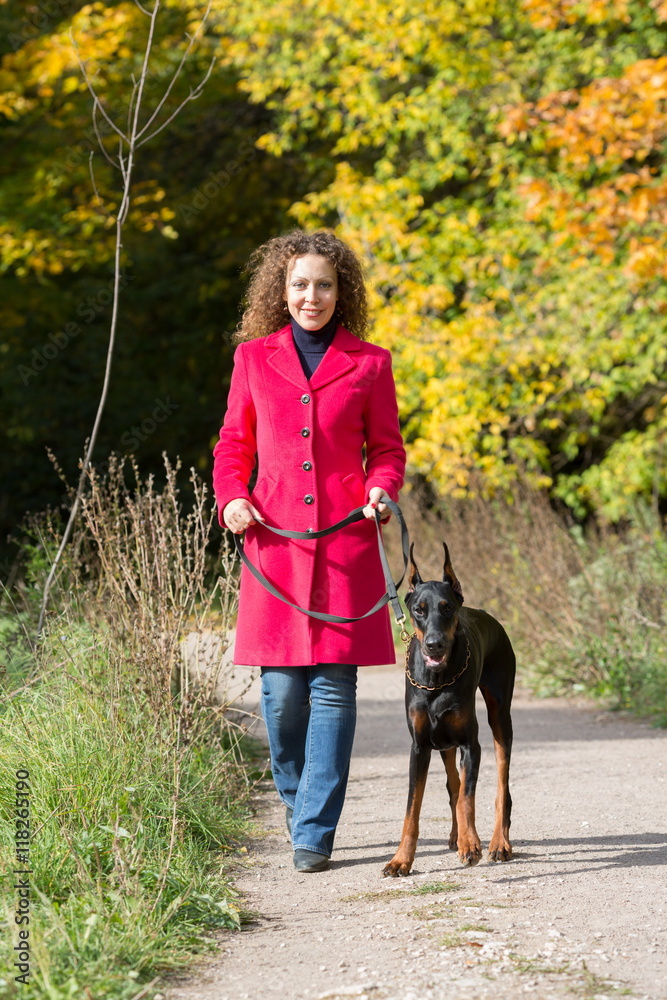 Smiling woman in a red coat is walking with the dobermann.