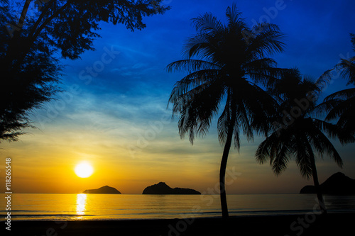Sunrise at sea with islands and coconut trees.
