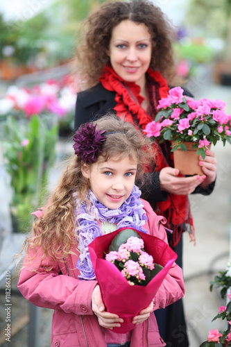Little girl with mother holding pot with beauty flowers in the greenhouse