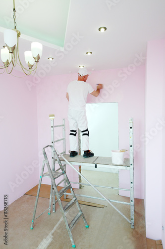 Finisher with brush in hand standing on scaffolding in pink room