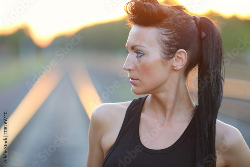 Portrait of a beautiful young girl in a black shirt on a railway track at sunset