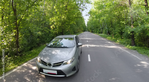 Car travels by road among trees with green foliage in forest at summer day. Aerial view