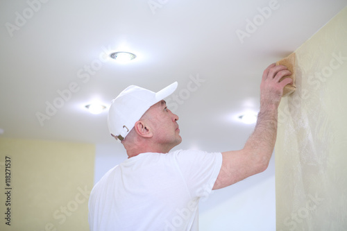 Finisher polishing the wall near the ceiling using a sanding sponge photo