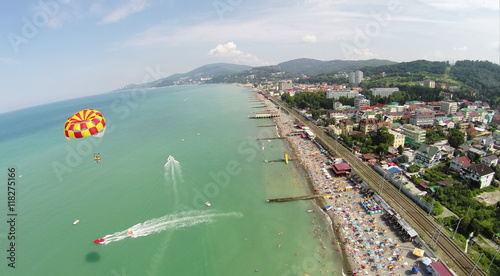 People fly by parachute near beach with many tourists at summer sunny day. Aerial view. Photo with noise from action camera.