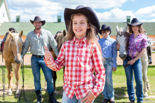 cowboy girl with ok gesture closeup portrait on background of her family with horses photo