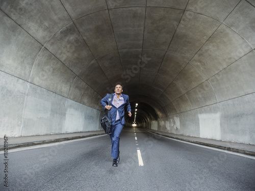 Black businessman running with briefcase in urban tunnel