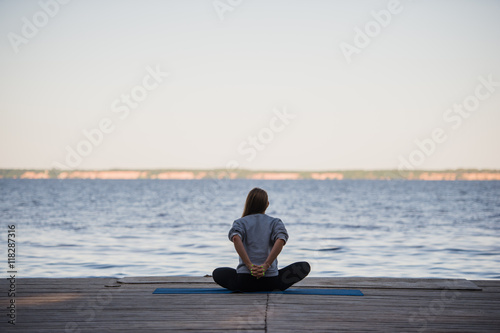 Woman doing stretching yoga exercises in the morning at the pier near sea or lake