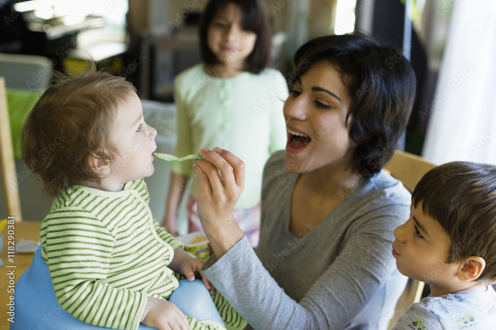 Hispanic mother feeding toddler in kitchen Hispanic mother feeding toddler in kitchen