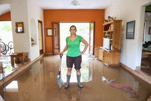 Hispanic woman shoveling water out of flooded house