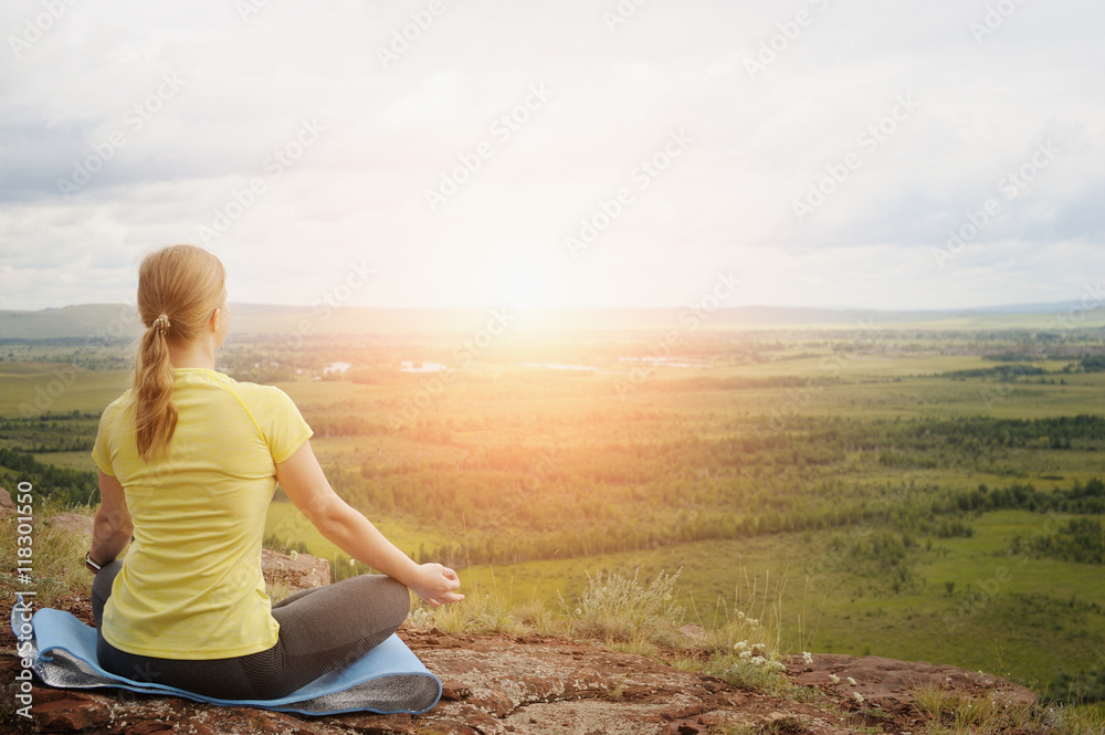 Woman in Lotus position on top of the mountain.