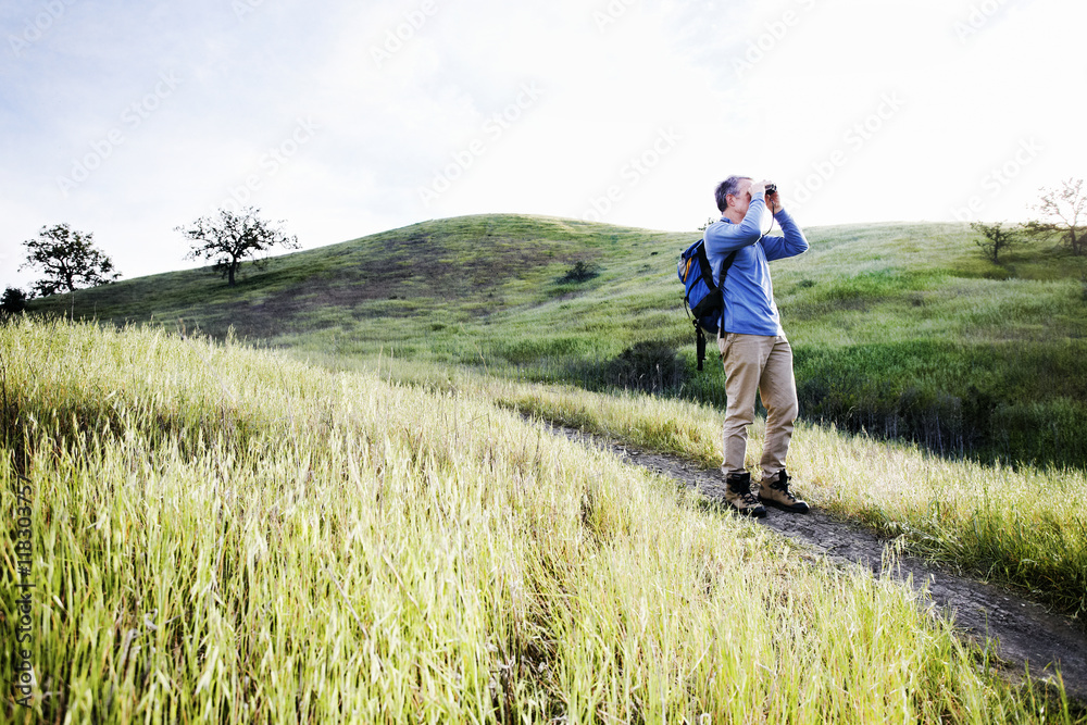 Caucasian man using binoculars on dirt path Caucasian man using binoculars on dirt path