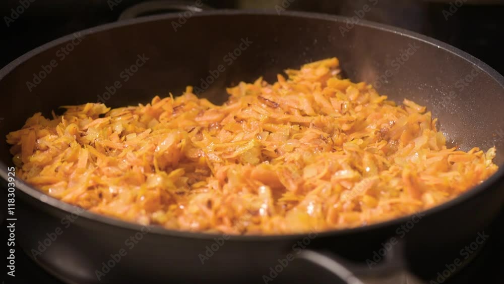 Chopped onions and carrots fried in vegetable oil in the pan. Close-up on top of a kitchen tile. Chopped onions and carrots fried in vegetable oil in the pan. Close-up on top of a kitchen tile.