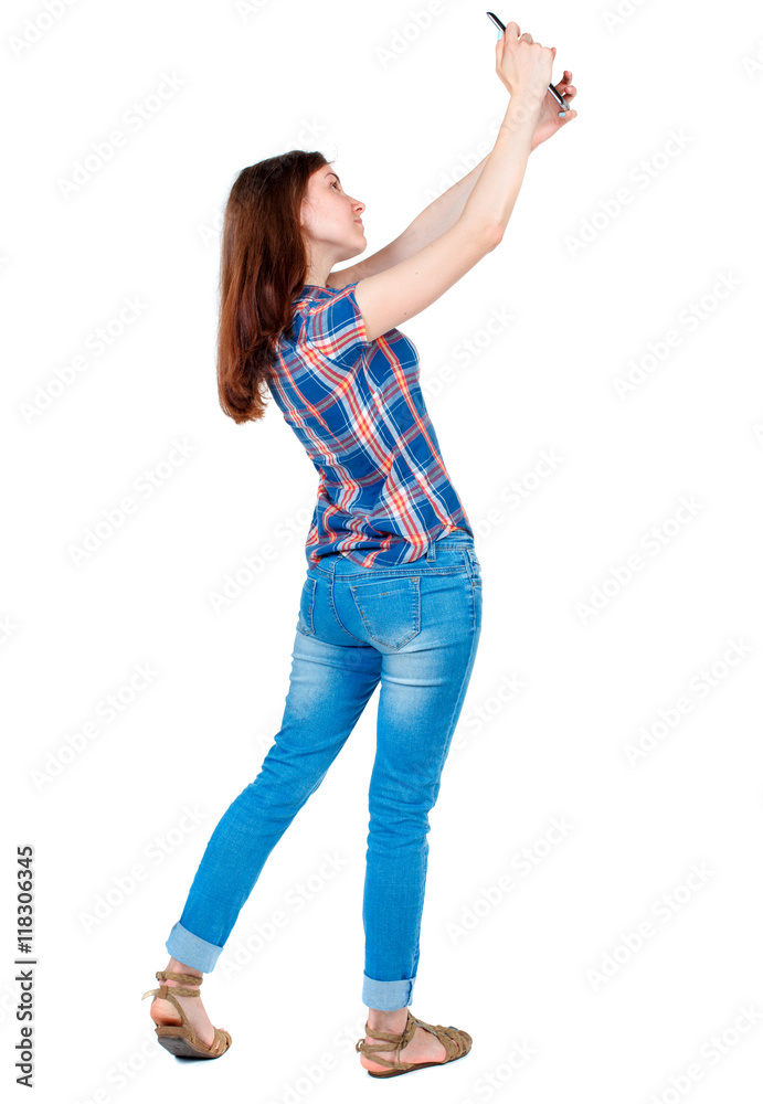 back view of standing young beautiful woman using a mobile phone. girl watching. Rear view people collection. backside view of person. Isolated over white background. Girl in plaid shirt standing back view of standing young beautiful woman using a mobile phone. girl watching. Rear view people collection. backside view of person. Isolated over white background. Girl in plaid shirt standing